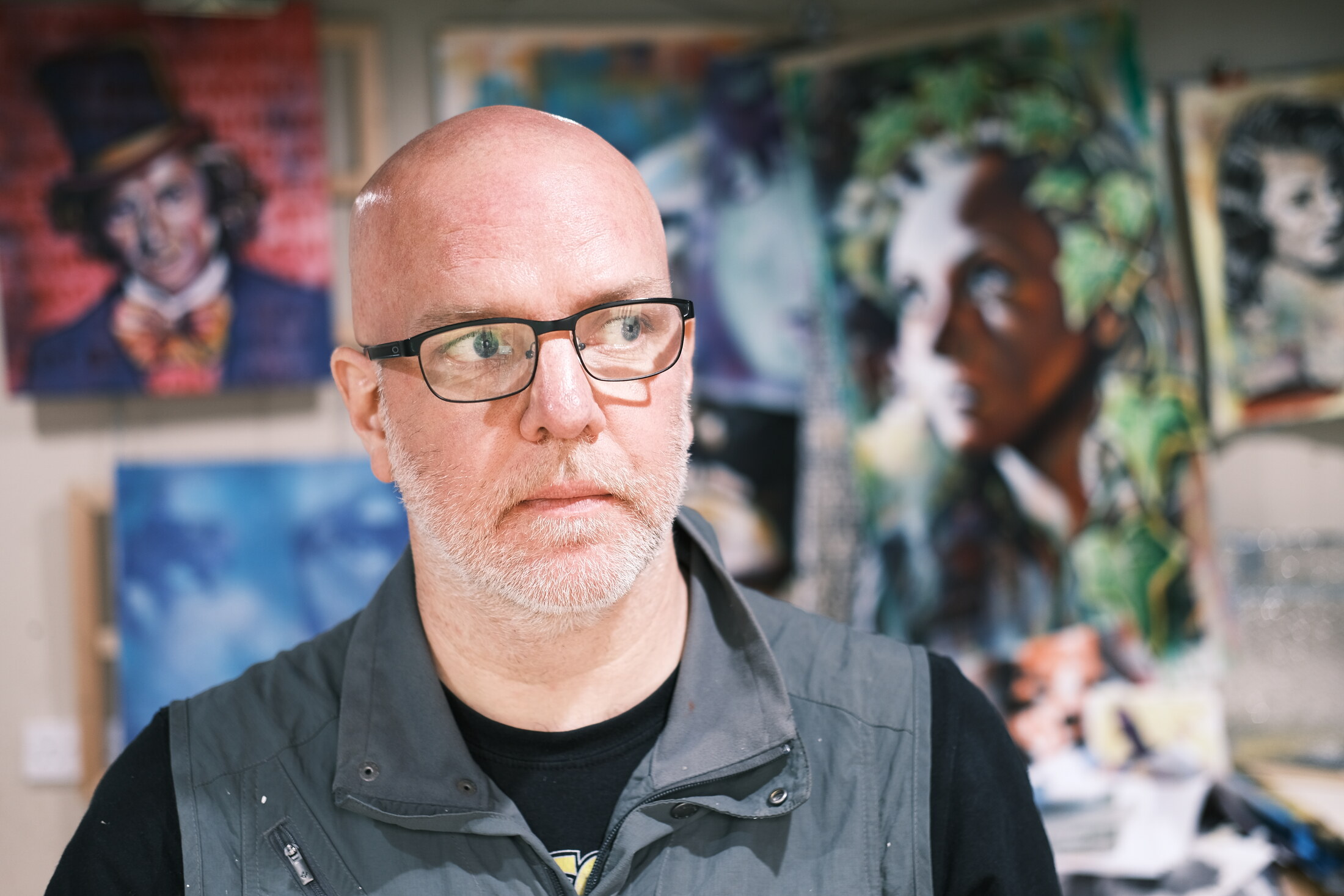 Alex Loveless leaning over a canvas in his studio, surrounded by paintings and art materials.